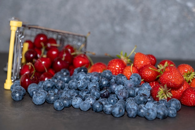 En un pequeño carrito de la compra de cerezas, arándanos y fresas sobre un fondo oscuro