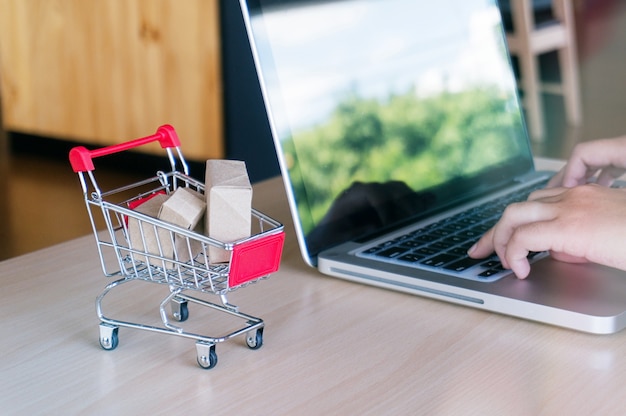 Pequeño carrito de la compra con el ordenador portátil para el concepto en línea de las compras.