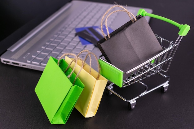 Foto pequeño carrito de compras con bolsas y computadora portátil concepto de compras en línea