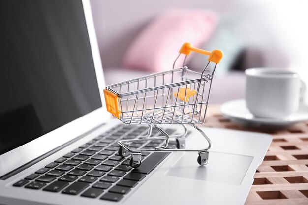 Pequeño carrito de compras y computadora portátil en la mesa closeup Concepto de compras por Internet