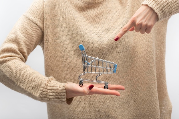 Pequeño carrito de compras en la mano femenina Señala con el dedo al carrito Concepto de venta