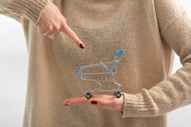 Pequeño carrito de compras en mano femenina Señala con el dedo al carrito