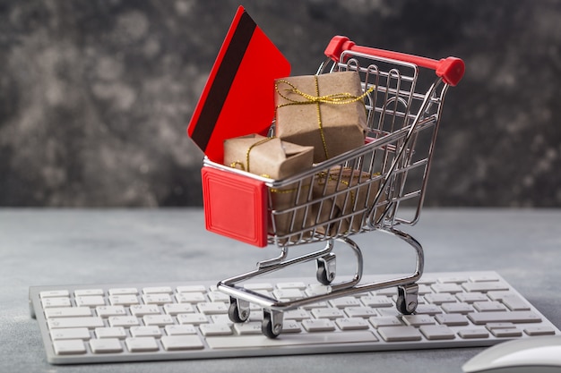 pequeño carrito de compras con regalos y tarjeta de crédito en un teclado portátil