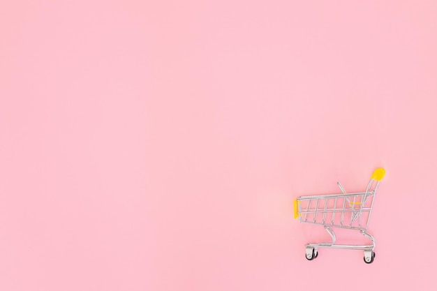 Pequeño carrito de compras sobre fondo rosa