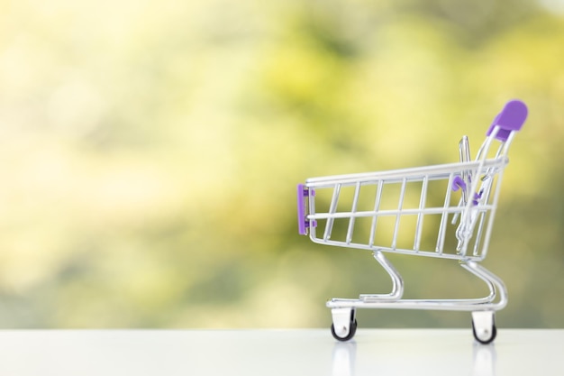 Pequeño carro de compras de juguete sobre fondo verde de verano Carro de compras vacío