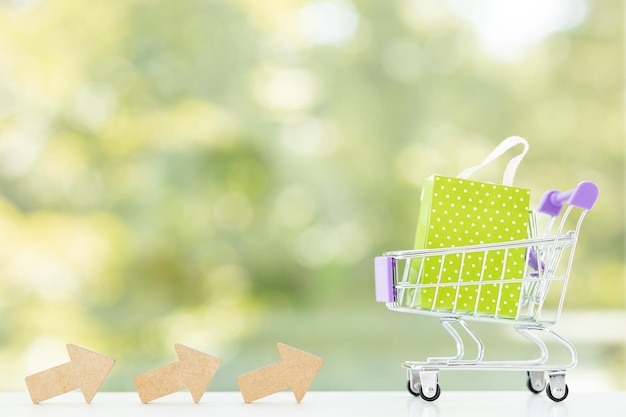 Pequeño carro de metal con bolsas de compras sobre fondo verde de verano