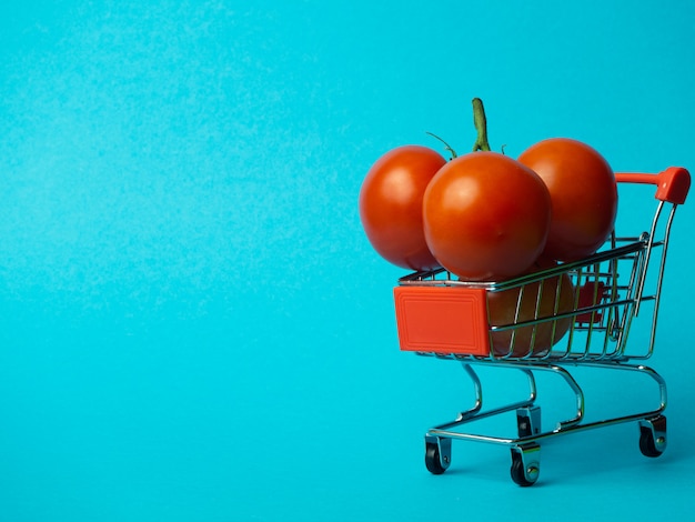 Pequeño carro con tomates sobre un fondo azul.