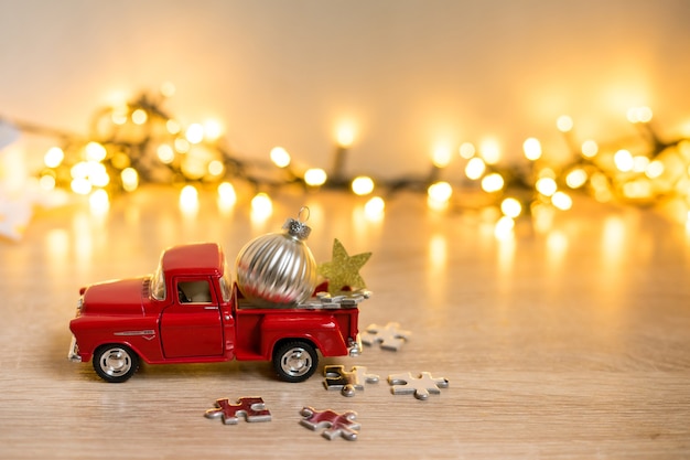 Pequeno carro vermelho brilhante decorativo de Natal em close-up sobre um fundo desfocado de decorações de Natal, luzes de guirlanda e bokeh. Foto de alta qualidade