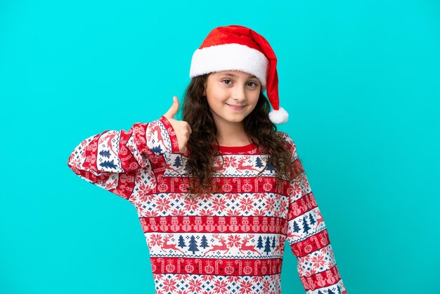 Pequeño caucásico con sombrero de navidad aislado de fondo azul con los pulgares hacia arriba porque algo bueno ha sucedido