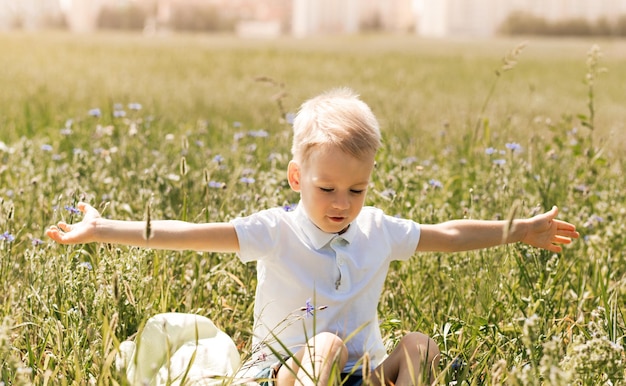 Un pequeño chico guapo rubio con una camisa blanca en la naturaleza en verano Infancia feliz Emociones positivas