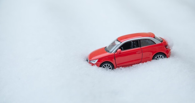 Pequeño coche de juguete rojo en la nieve en invierno