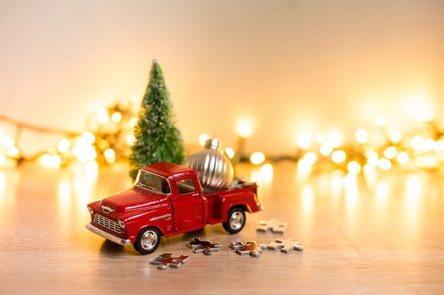 Pequeño coche rojo de Navidad brillante decorativo en primer plano sobre un fondo borroso de adornos navideños, guirnaldas y luces bokeh. Foto de alta calidad