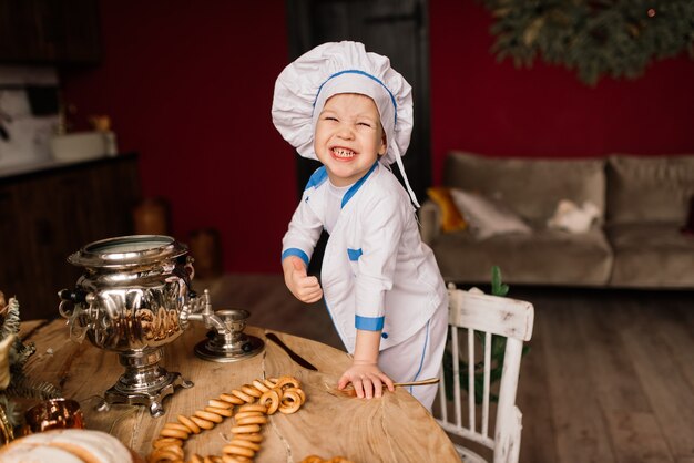 Pequeño cocinero lindo con cubiertos sentado en una cocina, hermanos gemelos, mandarina, bagels