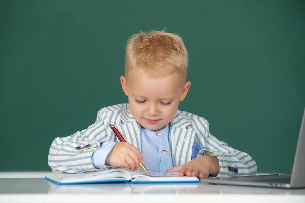 Pequeño colegial estudia en un salón de clases en un niño de escuela primaria escribiendo en clase