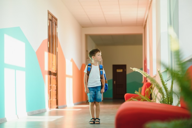 Pequeño colegial lindo sentado en el pasillo de la escuela