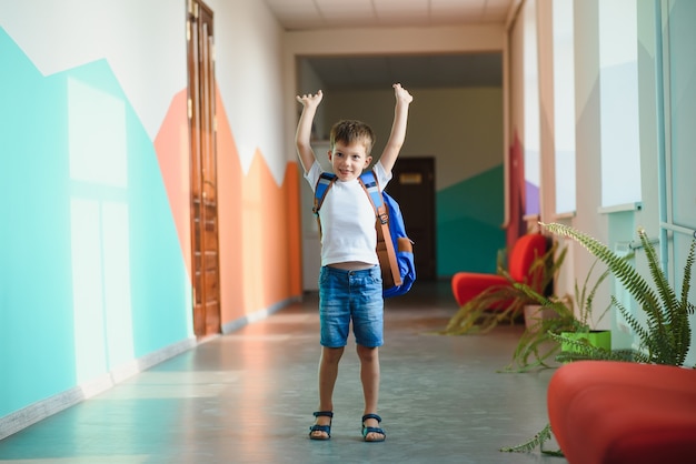 Pequeño colegial lindo sentado en el pasillo de la escuela