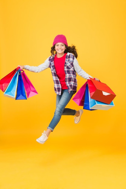 Pequeno comprador energético apressa-se à venda segurando sacos de compras loja de fundo amarelo