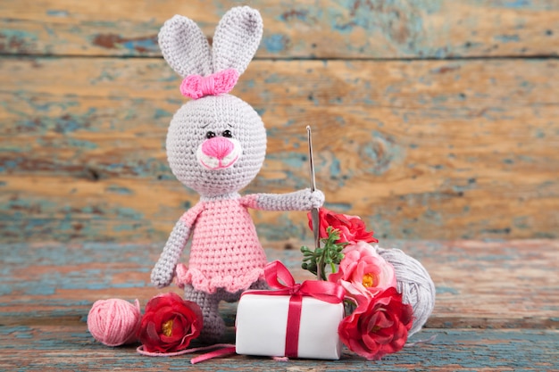 Un pequeño conejo gris hecho punto en un vestido rosado en un viejo fondo de madera. Juguete de punto, hecho a mano, costura.