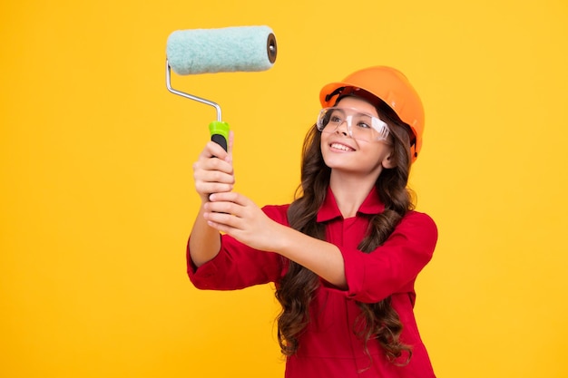 Pequeño constructor experto en casco en el sitio de construcción Pintor de niña adolescente con herramienta de pincel o rodillo de pintura Niño en trabajos de reparación Concepto de renovación Niña sonriente feliz