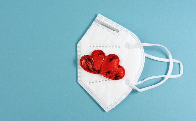 Pequeño corazón textil rojo se encuentra en una máscara médica desechable blanca, fondo azul