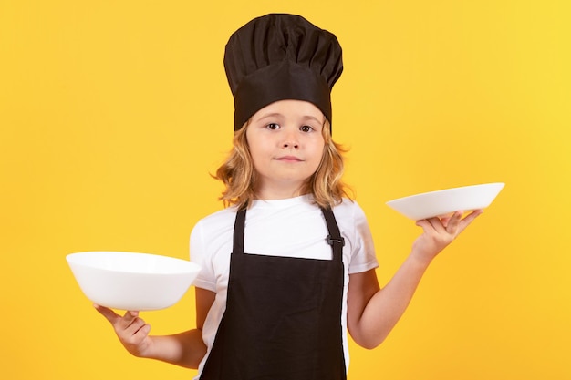 Pequeno cozinheiro com prato de cozinha Criança em uniforme de cozinheiro Chef garoto isolado em fundo amarelo Criança bonita para ser um chef Criança vestida como um chapéu de chef