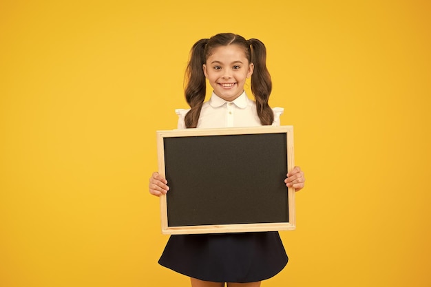 Pequeno criador de anúncios Criança segurando o quadro-negro no fundo amarelo Criança com quadro-negro para anúncio da escola Menina com quadro-negro vazio para o seu espaço de cópia de texto