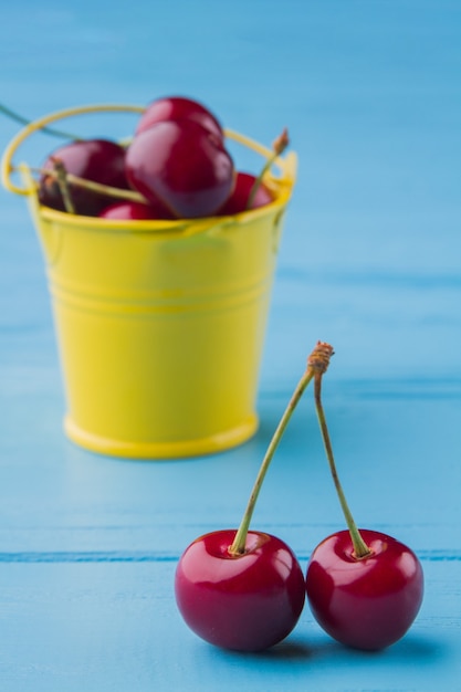 Foto pequeño cubo amarillo lleno de cerezas rojas frescas