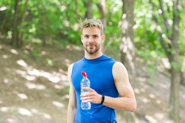 Pequeño descanso refrescante bebida vitamínica después del entrenamiento atlético hombre con botella de agua Atleta bebe agua después del entrenamiento en el cuidado del parque hidratación corporal deporte y salud hombre en ropa deportiva bebe agua