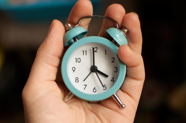 Un pequeño despertador azul que muestra 4 horas de tiempo en la mano sobre un fondo borroso