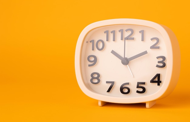 Pequeno despertador branco, números pretos, defina a hora colocada em uma mesa. relógio em fundo amarelo isolado.