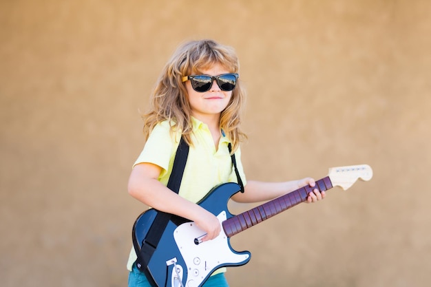 Pequeño y divertido músico hipster tocando la guitarra Niño rock divertido con guitarra Niño pequeño con gafas de sol Concepto de música para niños