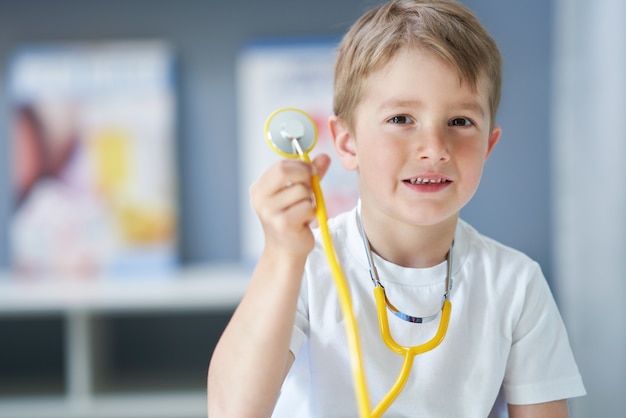 Pequeño doctor con estetoscopio sonriendo en el consultorio del médico