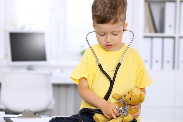 Pequeño doctor que examina a un paciente del oso del juguete por el estetoscopio