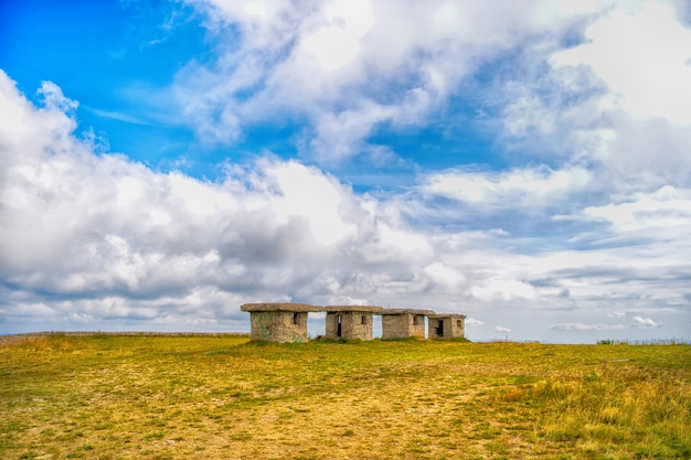 Pequeno edifício de pedra ou casinhas vazias no campo com grama verde e céu azul nublado ao ar livre em fundo natural