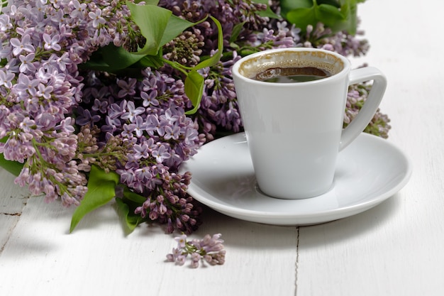 Pequeño y elegante ramo de flores de primavera y una taza de té en la mesa de madera blanca, desayuno de la mañana