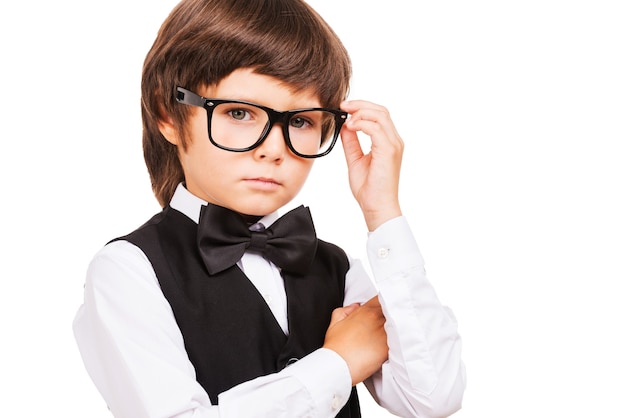 Pequeño empollón. Cute little boy ajustando sus gafas y mirando a la cámara mientras está de pie aislado en blanco