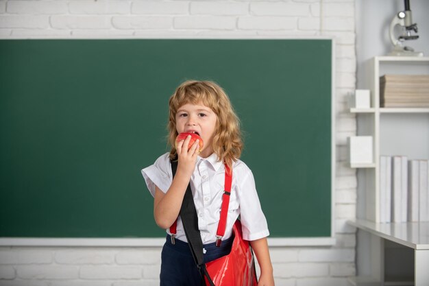 Pequeño estudiante de escuela comiendo manzana aprendiendo en clase estudiar inglés en la escuela Día del conocimiento del niño genio