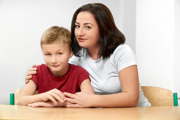 Pequeño estudiante masculino con madre y posando en el aula