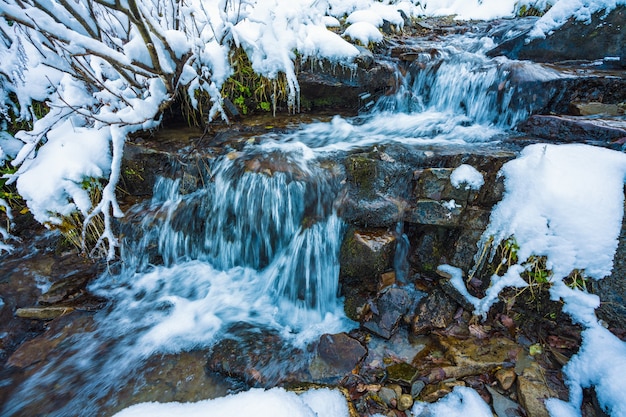 Pequeno fluxo rápido entre pequenas pedras molhadas e neve branca e fria nas pitorescas montanhas dos Cárpatos na bela Ucrânia e sua natureza fantástica