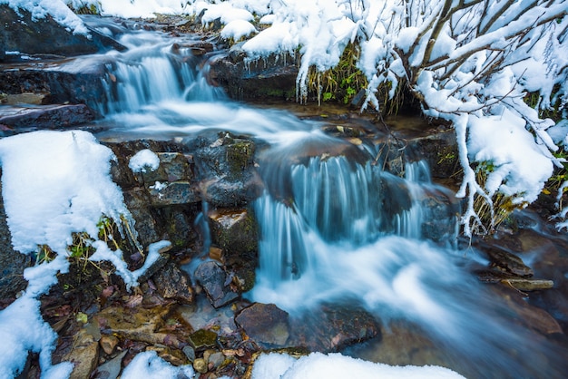 Pequeno fluxo rápido entre pequenas pedras úmidas e neve branca e fria nas pitorescas montanhas dos Cárpatos