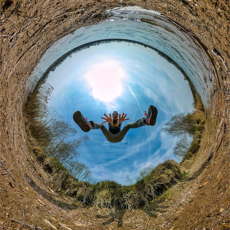 Foto pequeño formato de planeta de un hombre gestando mientras salta en la orilla del lago contra el cielo azul