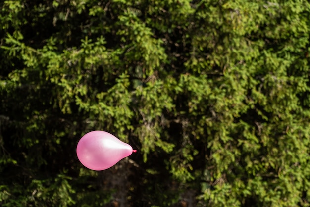 Pequeño globo rosa volando en el cielo con fondo verde bosque