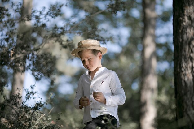 Pequeño granjero sonriendo y mirando a la cámara se encuentra en el bosque Niño lindo niño en un sombrero de paja