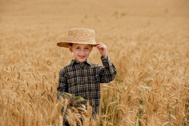 Un pequeño granjero sonriente con una camisa a cuadros y un sombrero de paja posa para una foto en un campo de trigo heredero o