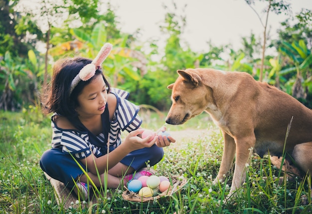 Pequeño gril lindo que lleva los oídos del conejito con los huevos y el perro de Pascua.