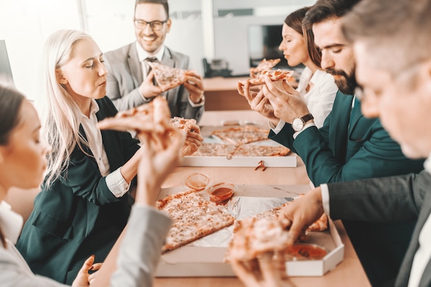 Pequeño grupo de colegas felices en ropa formal charlando y comiendo pizza juntos para el almuerzo. En lugar de intentar ser el mejor en el equipo, sé el mejor para el equipo.