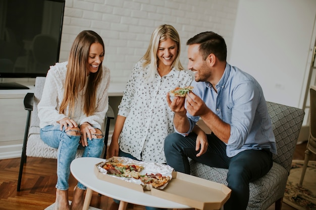 Pequeño grupo de jóvenes amigos comiendo pizza en la habitación