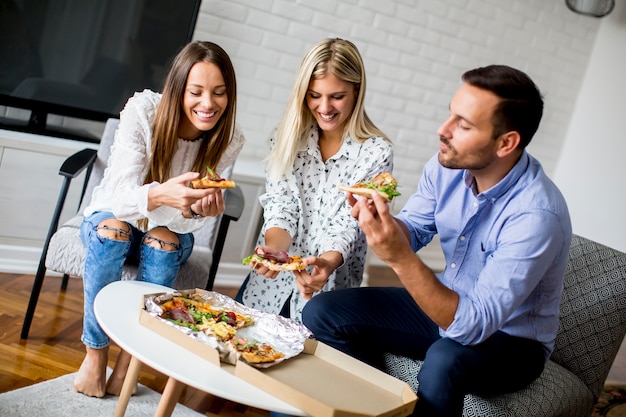 Pequeño grupo de jóvenes amigos comiendo pizza en la habitación