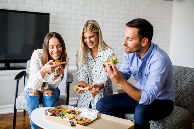 Pequeño grupo de jóvenes amigos comiendo pizza en la habitación