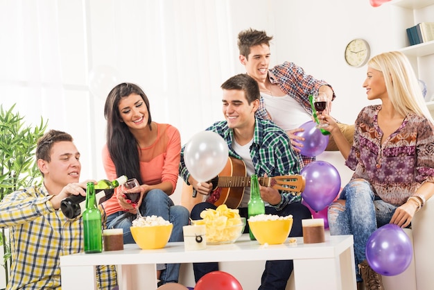 Un pequeño grupo de jóvenes en la fiesta casera, disfrutan de los sonidos de la guitarra acústica, bebiendo vino y cerveza.